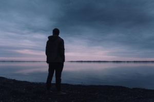 Man in grief stands looking out at water.